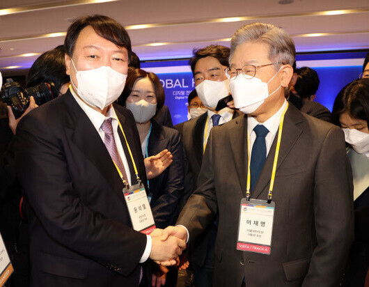 Democratic Party presidential nominee Lee Jae-myung (right) and People Power Party presidential nominee Yoon Seok-youl shake hands while at the Global HR Forum 2021 held by The Korean Economic Daily at the Grand Walkerhill Seoul hotel in Seoul’s Gwangjin District on Wednesday. (pool photo)