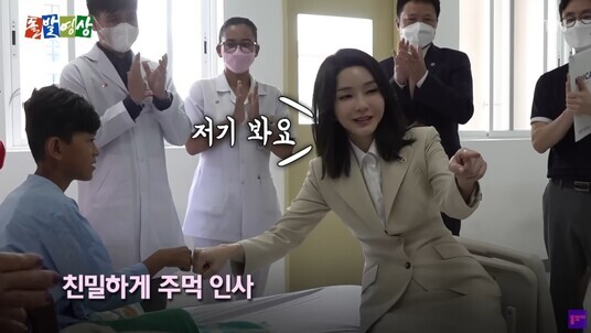 Still from a YTN program showing the first lady fist-bumping a boy in a hospital. Caption shows her saying, “Look over there.”