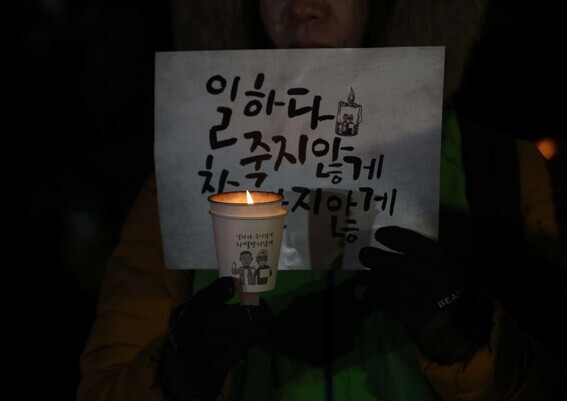 A person attending the one-year memorial of Kim Yong-gyun, a worker killed in an industrial accident, holds up a candle and sign at the rally on Dec. 7, 2019, in downtown Seoul. (Park Jong-shik/The Hankyoreh)