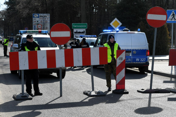 Polish officers stop traffic at the border crossing Ahlbeck - Swinemuende at the German-Polish border in Ahlbeck, Germany, Sunday, March 15, 2020. Poland has closed the borders for all foreigners since Sunday morning because of the novel coronavirus outbreak. For most people, the new coronavirus causes only mild or moderate symptoms, such as fever and cough. For some, especially older adults and people with existing health problems, it can cause more severe illness, including pneumonia. (dpa via AP)