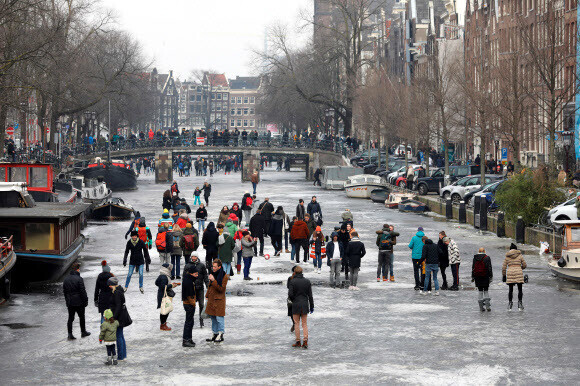 Amsterdam residents frolic on a frozen canal as some skate and others take snapshots on Jan. 3. (Reuters/Yonhap)