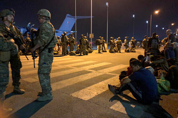 French soldiers stand guard as French and Afghan nationals wait to board a military transport plane at the airport in Kabul on Tuesday. (AFP/Yonhap News)