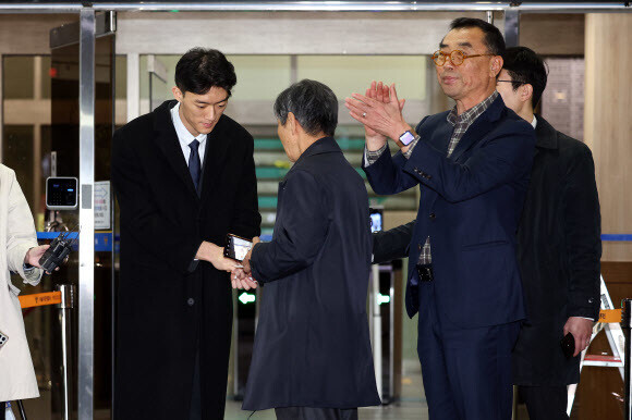 Chun Woo-won, the grandson of Chun Doo-hwan, shakes hands with Jeon Tae-sam, the brother of labor martyr Jeon Tae-il. To their right, the president of the May 18 Memorial Injured’s Seoul branch applauds Chun. (Yonhap)