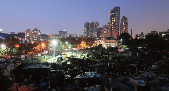 2011년 6월 폐기물 야적장에 난 불로 잿더미가 된 서울 강남구 포이동 1226번지 재건마을의 어둠 뒤로 타워팰리스 등 고층 주상복합건물이 불빛을 뽐내고 있다. 한겨레 신소영 기자