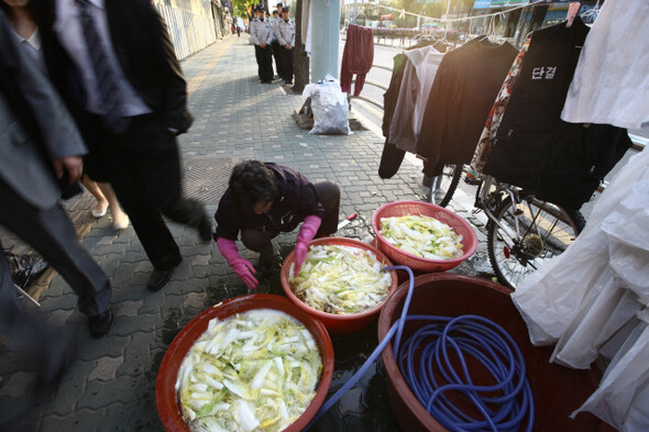 참사 현장인 남일당 건물에서 농성 중인 유족 가운데 한 아주머니가 김치를 담그기 위해 소금에 절인 배추를 씻고 있다. 옆으로 퇴근하는 직장인들이 지나가고 있다.
