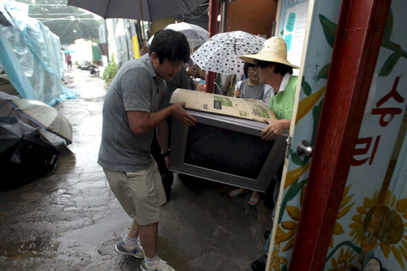 » 지난 7월7일 서울 포이동 판자촌 화재사고 현장을 방문한 사회당원들이 쏟아지는 빗줄기를 뚫고 위문품으로 가져온 텔레비전을 운반하고 있다. 한겨레21 이종찬 