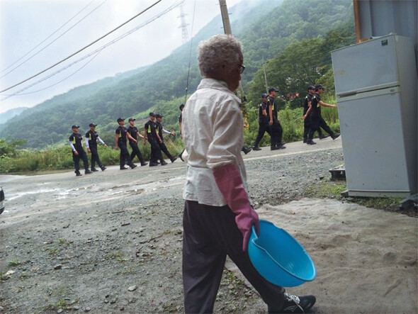 대열을 맞춘 경찰들이 7월14일 점심 식사를 하기 위해 평밭마을(경남 밀양시 부북면 대항리) 사랑방(새 농성장)을 지나 마을로 올라가고 있다. 6월11일 송전탑 반대 농성장 행정대집행 이후 경찰들은 마을 안 식당에서 밥을 먹고 있다. 연세통 제공