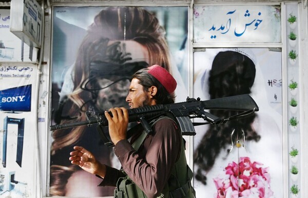 A Taliban fighter walks past a beauty salon with images of women sprayed over in Kabul, Afghanistan, on Aug. 18. (AFP/Yonhap News)