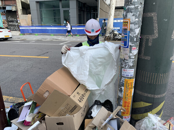 A 66-year-old sanitation worker, K, looks through trash left along the curbs of a street in Itaewon. (Kim Yoon-ju/The Hankyoreh)