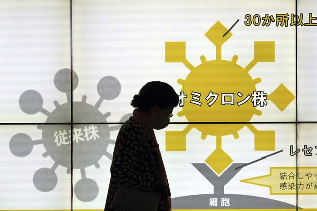 마스크를 쓴 여성이 13일 일본 도쿄에서 오미크론 변이 확산을 경고하는 표지판 앞을 지나고 있다. 도쿄/AP 연합뉴스