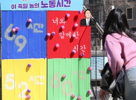 Members of the Korean Confederation of Trade Unions survey office workers in downtown Seoul on March 22 and have them throw balls at a board with the different numbers of weekly working hours proposed by the Yoon administration. (Shin So-young/The Hankyoreh)