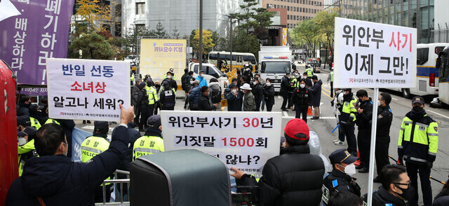 Groups hold up signs while protesting the 1,517th iteration of the Wednesday Demonstration aimed at resolving the issue of the Japanese military’s system of sexual enslavement on Nov. 10, 2021, in front of the offices of Yonhap News in Seoul’s Jongno District. (Kim Hye-yun/The Hankyoreh)