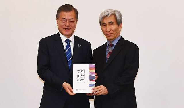 President Moon Jae-in holds a copy of the draft constitutional amendment alongside Jung Hae-gu