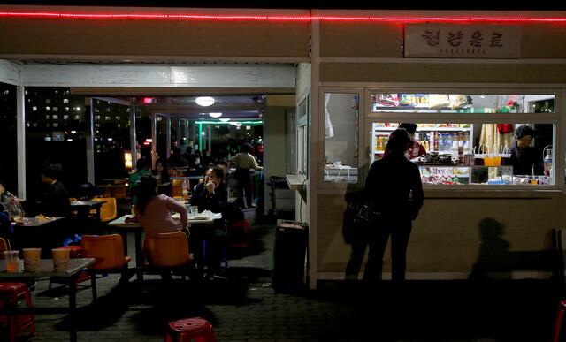 Pyongyang residents enjoy beer and snacks in street markets during nighttime in front of Kaeson Youth Park. (provided by Unification TV)