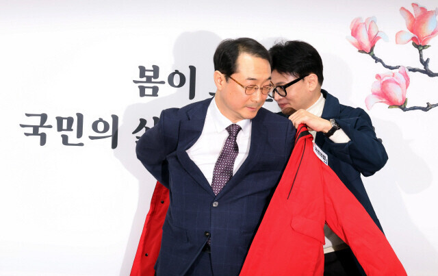 Han Dong-hoon, interim leader of the People Power Party, helps Kim Geon, then director of the Office of Korean Peninsula Peace and Security Affairs, into a party jacket during a ceremony for recruiting new members at the party's Seoul headquarters on Feb. 29. (Kim Gyoung-ho/The Hankyoreh)