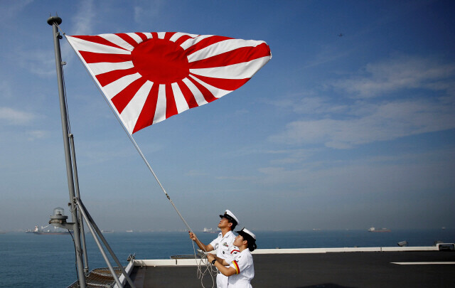Two JSDF members hoist the “Rising Sun” flag on a warship. (Yonhap)