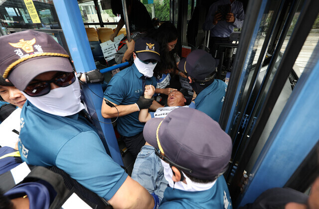 Police drag Solidarity Against Disability Discrimination co-representative Lee Gyu-sik out of a bus at Seoul’s Hyehwa Rotary on July 17, 2023, as he protests for fair access to public transport for disabled people. (Yonhap)