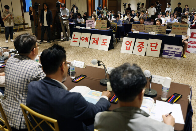 During a public hearing on the plan for a pilot program for foreign domestic help held at the Royal Hotel Seoul on July 31, civic groups display placards reading “Stop the introduction of a slavery system.” (Yonhap)