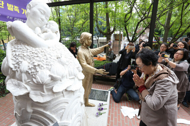 Former comfort women Lee Yong-su clasps her hands as she kneels after placing flowers in front of a scale of the pieta statue for victims of the Vietnam War in front of the Franciscan Education Center in Seoul