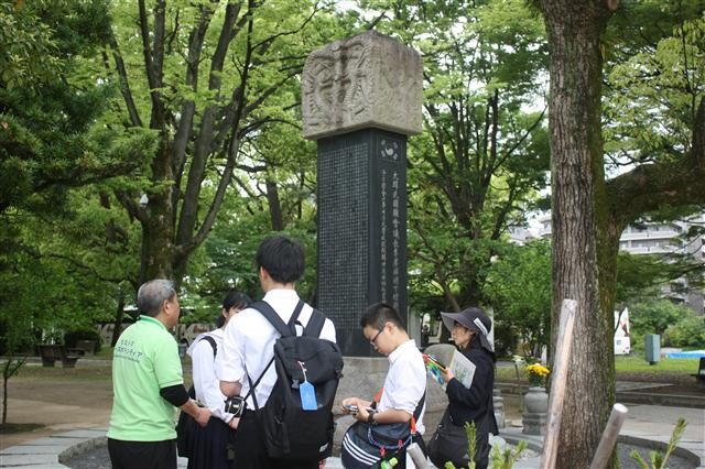 Japanese visitors to Hiroshima Peace Park listen to a guide’s explanation at the memorial stone to Korean victims of the bombing