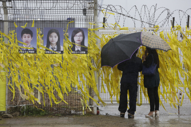비가 내린 4월5일, 추모객들이 미수습자 사진이 걸린 곳에서 세월호를 바라보고 있다.