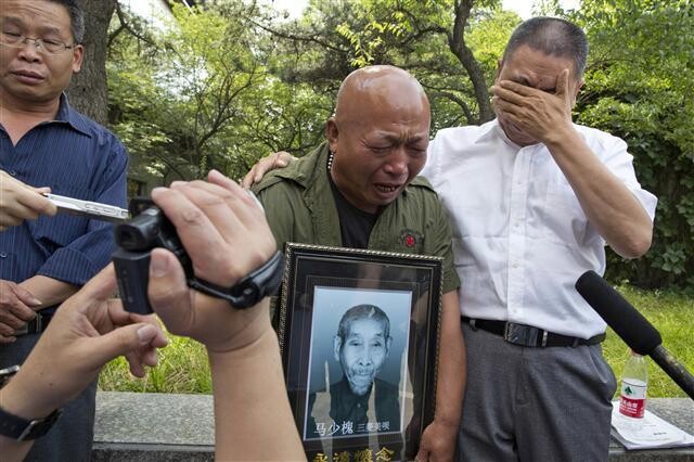 The son of a victim of forced labor by the Japanese company Mitsubishi Materials (formerly Mitsubishi Mining) weeps during an interview in Beijing while holding a photograph of his father after the company agreed to pay reparations of 100