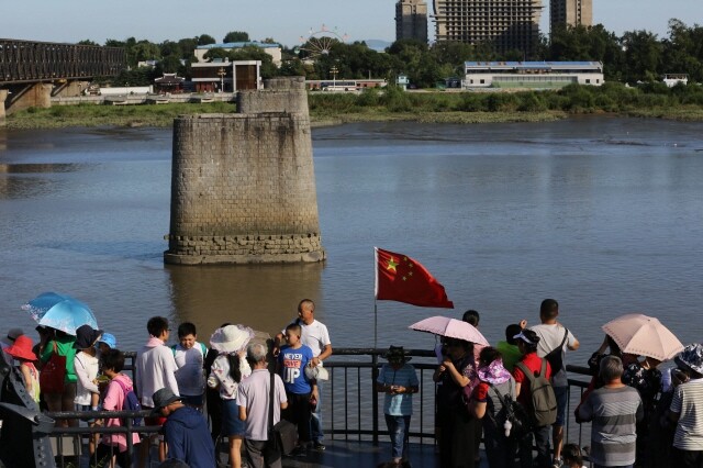 Chinese tourists pose for photographs in front of the remains of a bridge that once connected the Chinese city of Dandong with the North Korean city of Sinuiju on Nov. 8. (Kim Bong-gyu