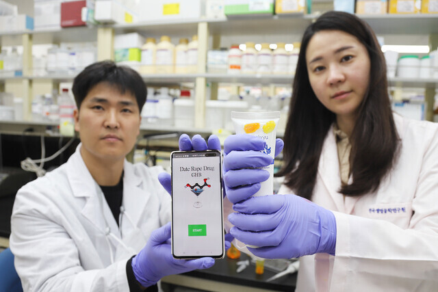 Kwon Oh-seok, a senior researcher at the Infectious Disease Research Center of the Korea Research Institute of Bioscience & Biotechnology, and researcher Kim Jin-yeong hold up a gel that detects the “date rape” drug GHB via color change, and an app that helps decern the color changes in low light scenarios. (provided by the Korea Research Institute of Bioscience & Biotechnology)