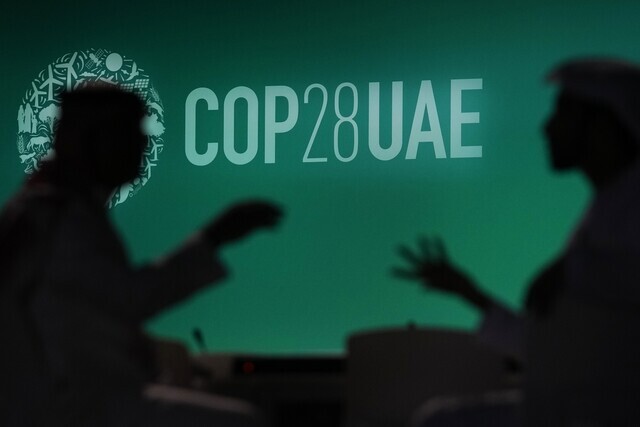 Two people speak to one another against the backdrop of the COP28 logo on Nov. 29 ahead of the climate summit’s kickoff in Dubai, United Arab Emirates. (AP/Yonhap)