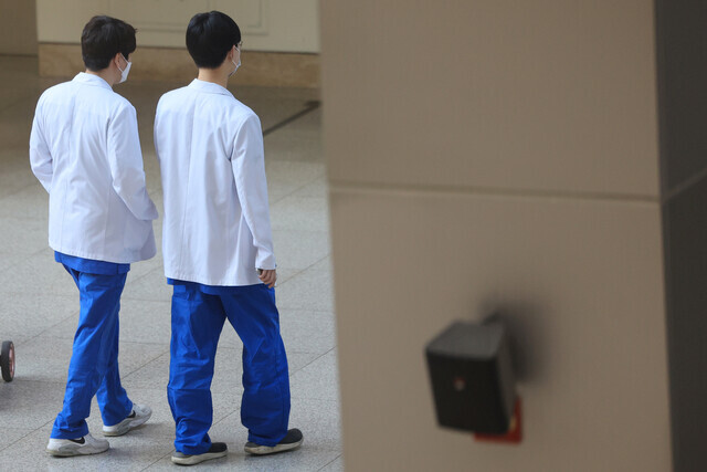 Two medics in white coats and scrubs walk through a university hospital in Seoul on March 21, 2024, amid a ratcheting up of tensions between medical school faculty and the Korean government over an increase in medical school placements. (Yonhap)