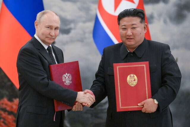 Russian President Vladimir Putin (left) and North Korean leader Kim Jong-un shake hands while holding copies of their newly signed pact establishing a comprehensive strategic partnership between their two nations following their summit in Pyongyang, North Korea, on June 19, 2024. (TASS/Yonhap)