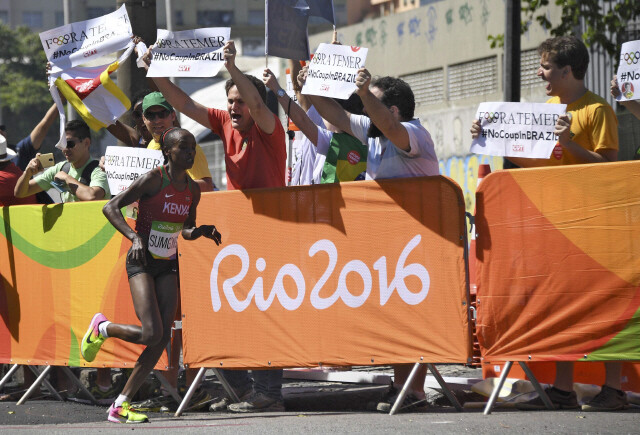 8월14일 브라질 리우데자네이루올림픽 여자마라톤에서 금메달을 딴 케냐의 제미마 숨공이 역주하는 모습. 그 옆에서 브라질 시민들이 ‘테메르 퇴진, 쿠데타 반대’라고 쓴 종이를 들고 시위하고 있다. REUTERS