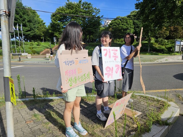 1.5도 라이프스타일 한 달 살기 참가자인 이봄(가운데)씨가 2024년 7월25일 경남 진주시 개양오거리에서 기후 관련 시위를 하고 있다. 이날 시위에는 이씨와 같은 간디고등학교 학생인 김여영(17)씨와 조현수(18)씨가 함께했다. 류석우 기자