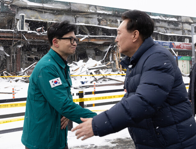 Han Dong-hoon, the interim leader of the People Power Party (left), shakes hands with President Yoon Suk-yeol as the two jointly inspect on Jan. 23 the site of a fire that destroyed a marine products market in Seocheon, South Chungcheong Province, the night before. (courtesy of the presidential office)