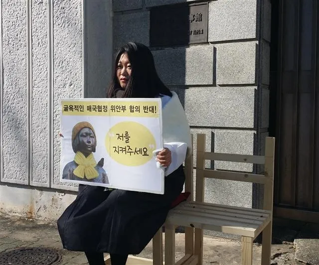 A young woman holds a sign saying “Protect me” while taking part in a human statue relay protesting the recent South Korea-Japan comfort women settlement in front of the Japanese consulate in Busan. Busan has no comfort woman statue like the one opposite the Japanese embassy in Seoul