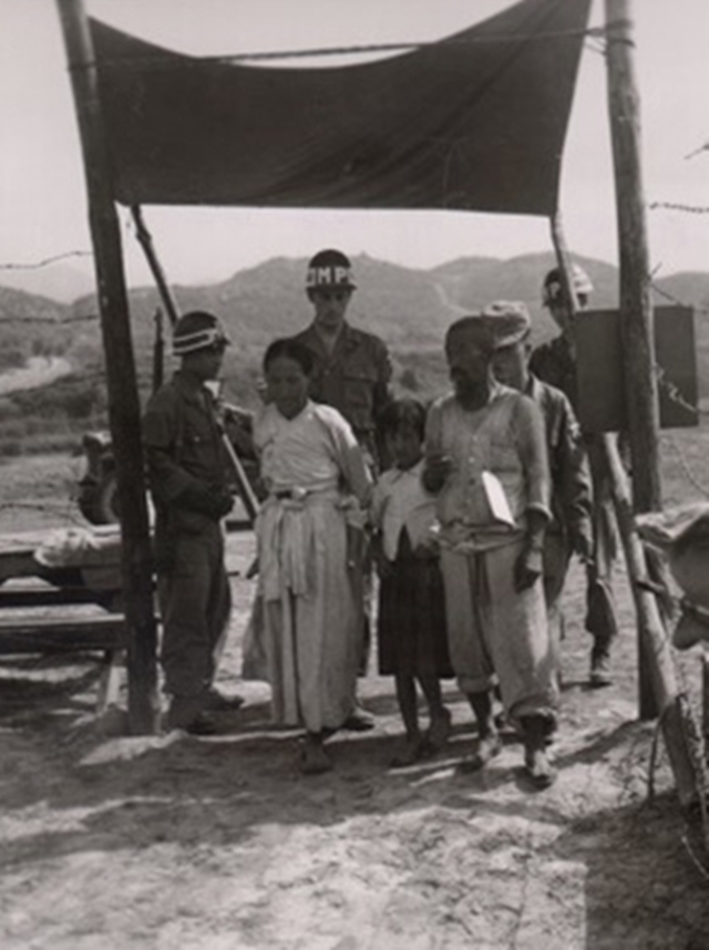 ❸조사와 심문을 받은 피란민들이 포로구역에서 신원 승인과 그들을 인수할 민사장교를 기다린다. 평균 대기시간은 24시간이다. 피란민은 포로구역에 있는 동안 하루 두 번 식사를 받는다. 1951년 7월19일 매키니 촬영.