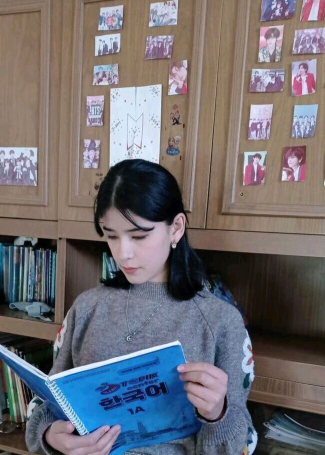Anna from Uzbekistan reads a Korean textbook. On the wall behind her are photos of the K-pop boy group BTS. (courtesy of Anna)