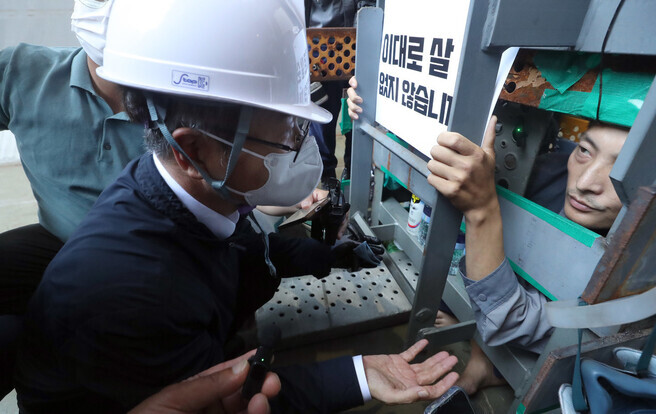 Employment and Labor Minister Lee Jung-sik (left, in hardhat) speaks to Yu Choe-an, the deputy head of the shipbuilding subcontractors union branch who is currently staging a sit-in in a 1-cubic-meter metal box on the main dock of a shipyard in Geoje, on July 19, the 28th day of the sit-in. (pool photo)