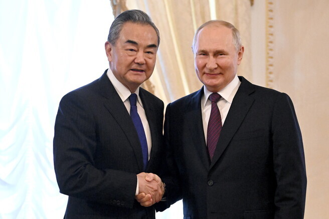 Chinese Foreign Minister Wang Yi (left) shakes hands with Russian President Vladimir Putin during their meeting in St. Petersburg on Sept. 20. (TASS/Yonhap)