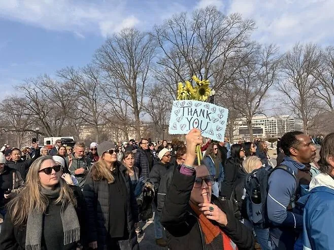 Debbie Evans of Delaware raises a bouquet of yellow flowers and a sign reading “Thank you” as she marches with others following the