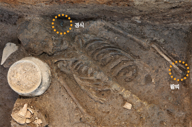 Remains of a woman recently discovered during additional surveys of Wolseong Palace’s western wall, in Gyeongju, are pictured. The two circles highlight a necklace and a bracelet. An earthen pot can be seen on the left. (provided by the Gyeongju National Research Institute of Cultural Heritage)