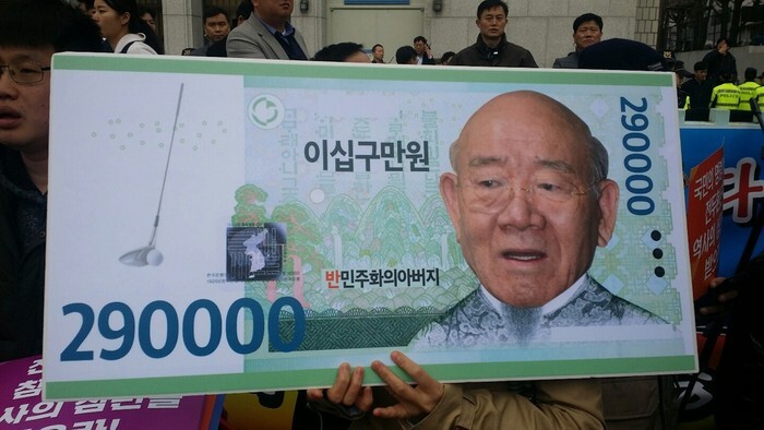 Activists hold up a placard mocking former President Chun Doo-hwan, who claimed that his assets totaled to less than US0 during his trial. (Hankyoreh archives)