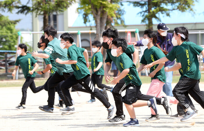 Students in masks run on a soccer field at an elementary school in Seoul. (Yonhap)