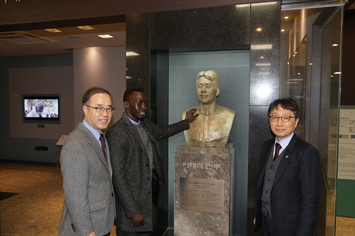 Taban Akot in front of a bust of the late Father Lee Tae-seok with Inje University President Kim Sung-soo (left) and Lee Jong-tae