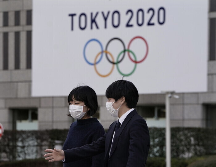 Two people wearing masks walk past a banner for the Tokyo 2020 Olympic and Paralympic Games. (EPA/Yonhap News)