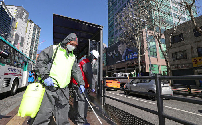 On Mar. 11, sanitation workers disinfect a bus stop near a call center in Seoul’s Guro District where a novel coronavirus transmission cluster was discovered. (Yonhap News)