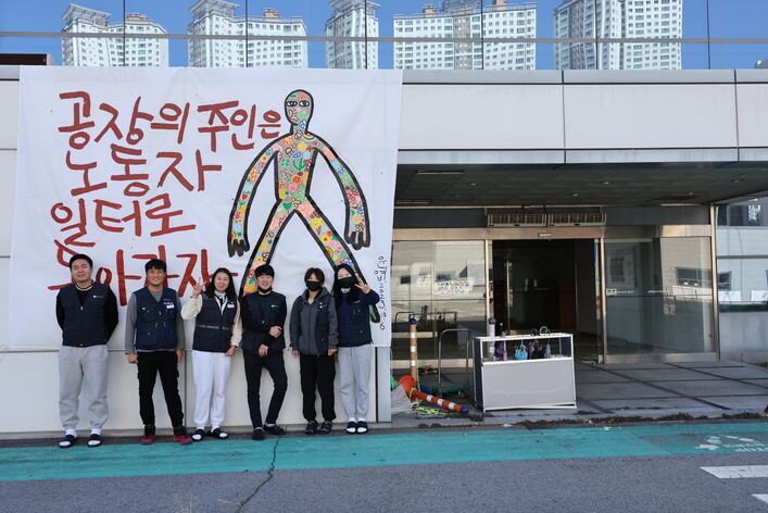 금속노조 한국옵티칼하이데크지회 조합원들이 2023년 11월13일 불 탄 구미공장 앞에 서 있다. 류우종 기자