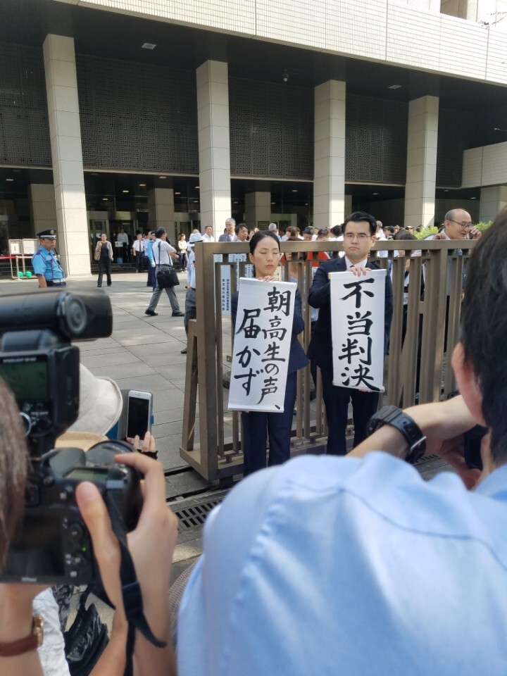 Attorneys for a group of Chosen Gakko students hold signs reading “Unfair judgment” and “The students voices aren’t behind heard” outside of the Tokyo District Court after a ruling was issued allowing the government to deny subsidies to the pro-North Korean school on Sept 13.