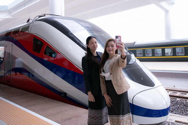 Two women take a photo in front of the newly adopted electric train at a high-speed train station in the capital of Laos, Vientiane, on Oct. 16. This railway project that connects Vientiane and Kunming, China, was pursued as part of China’s Belt and Road Initiative, and has left the Laos government with a substantial amount of debt on their shoulders. (Xinhua/Yonhap News)