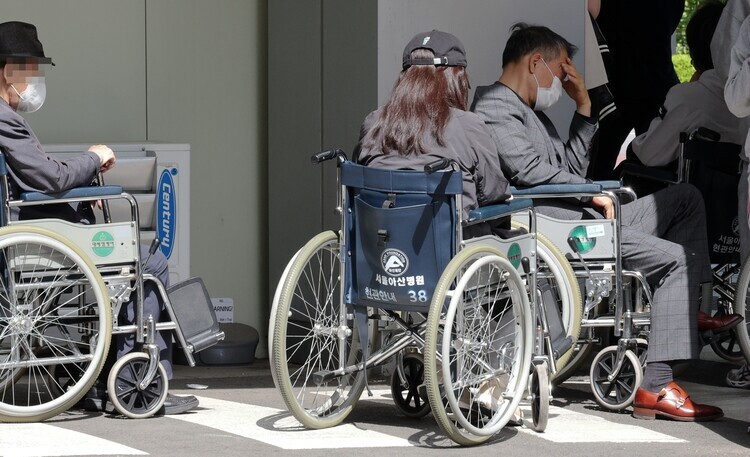 Patients wait in line for treatment in wheelchairs outside the emergency room at Seoul’s Asan Medical Center on April 18, 2024, the two-month mark in the ongoing standoff between Korea’s junior doctors and government. (Kim Jung-hyo/The Hankyoreh)